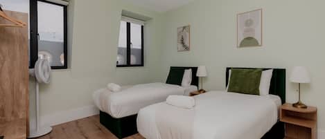 A hotel room with two beds, a fan, a window, and a view of the sea.