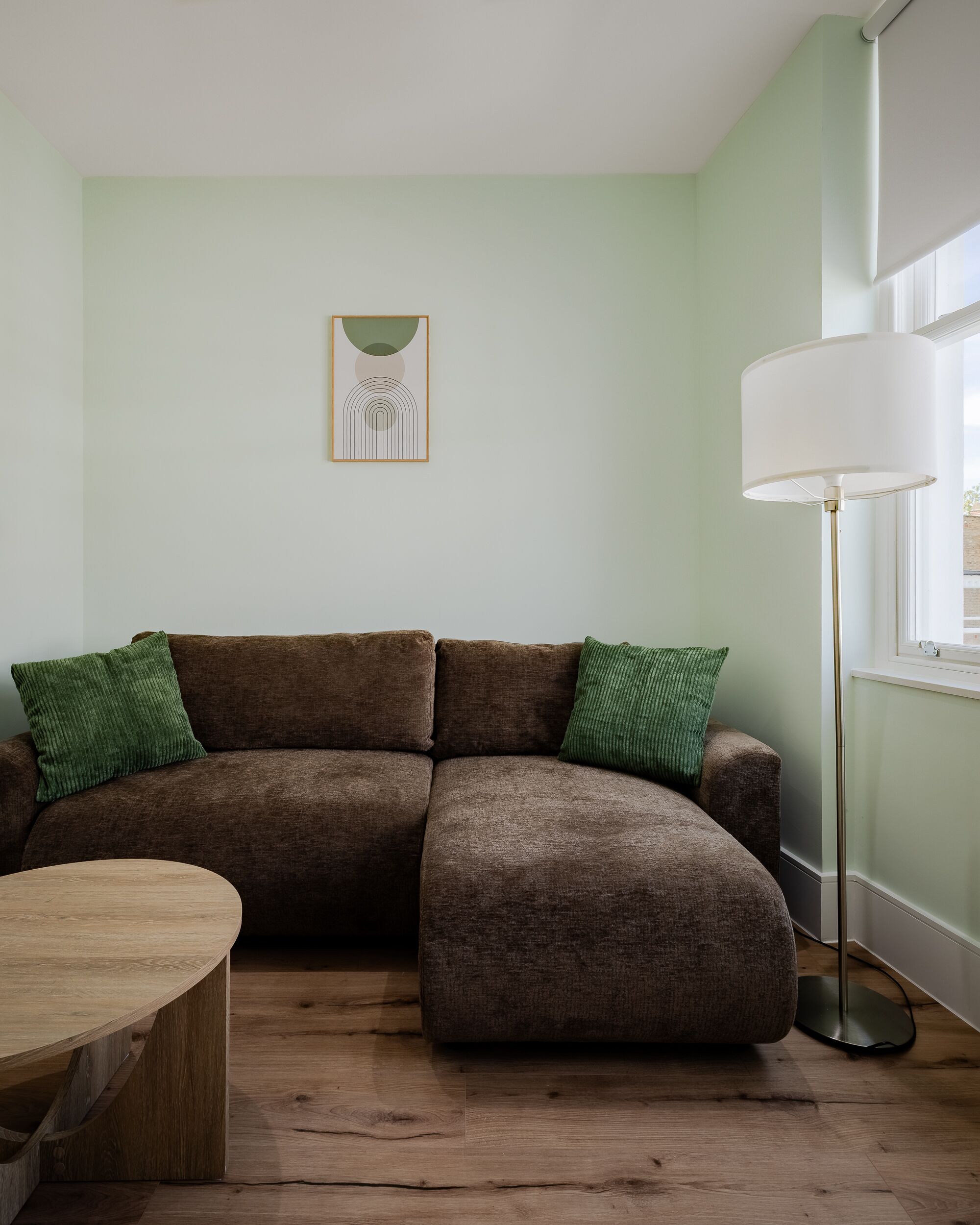 A living room with a brown sectional sofa, a wooden coffee table, a floor lamp, and a framed abstract artwork on the wall.