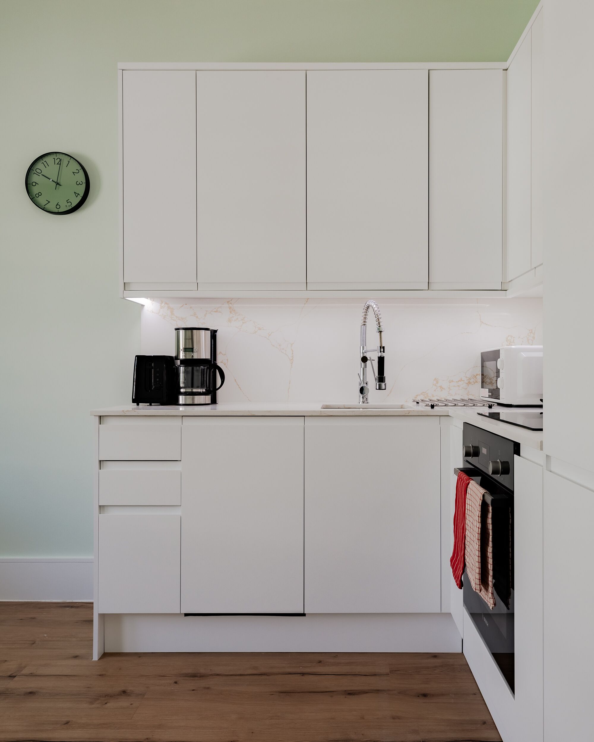 A modern kitchen with white cabinetry, a coffee maker, a sink, and an oven.
