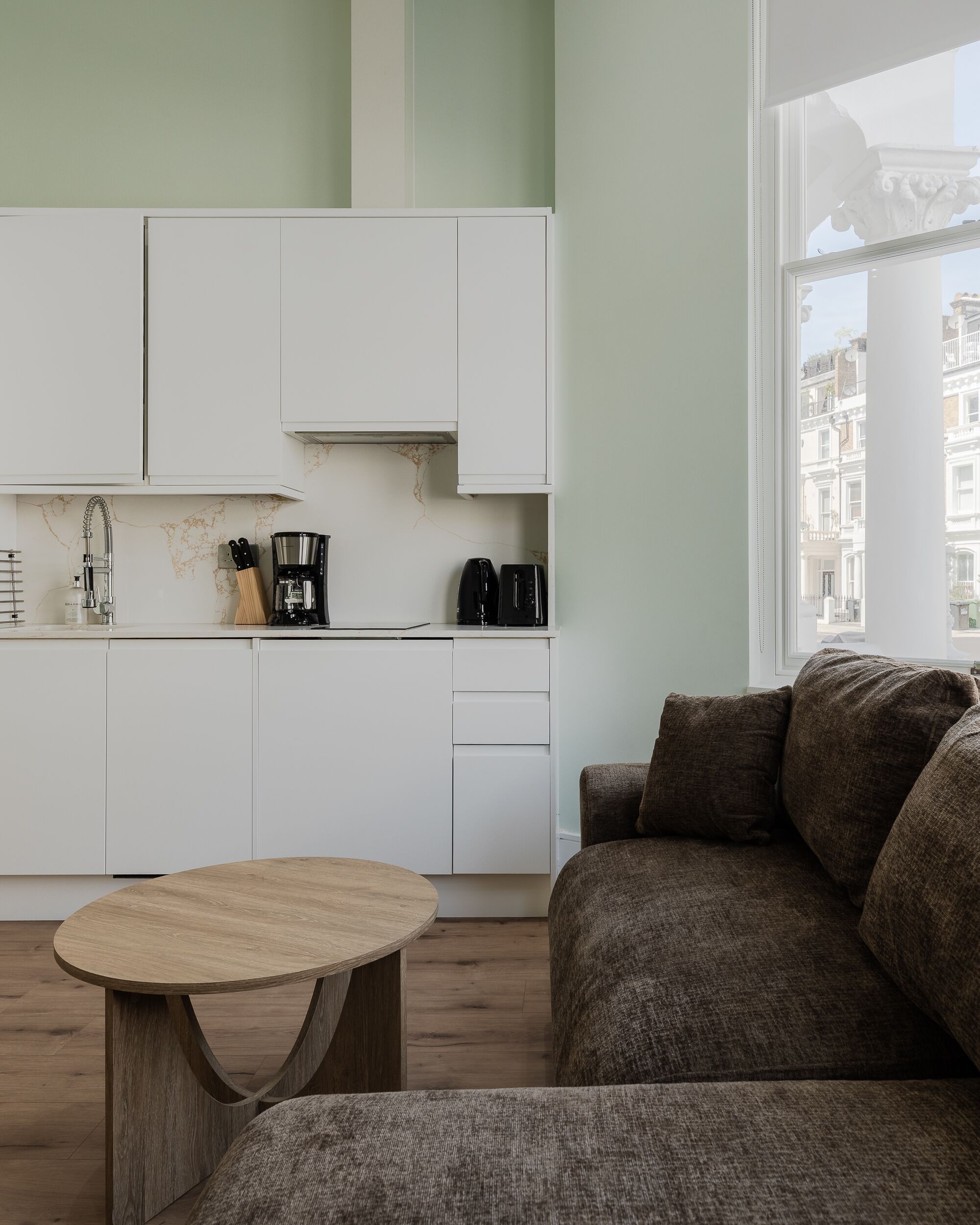 A modern kitchen with white cabinets, a coffee maker, and a view of buildings through a window.