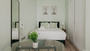 A hotel room with a bed, bedside table, lamp, and a mirror reflecting the room. - Olympia Grand Apartments (London)