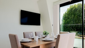 A dining area with a wooden table, four chairs, and a TV mounted on the wall. - Olympia Grand Apartments (London)