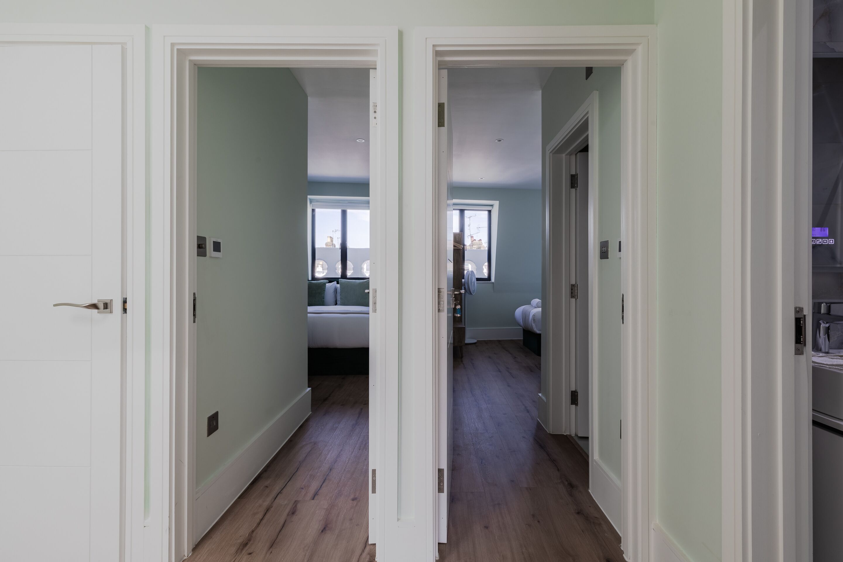 Ein Flur mit weißen Türen, der zu einem Schlafzimmer mit Bett und Fenster führt.