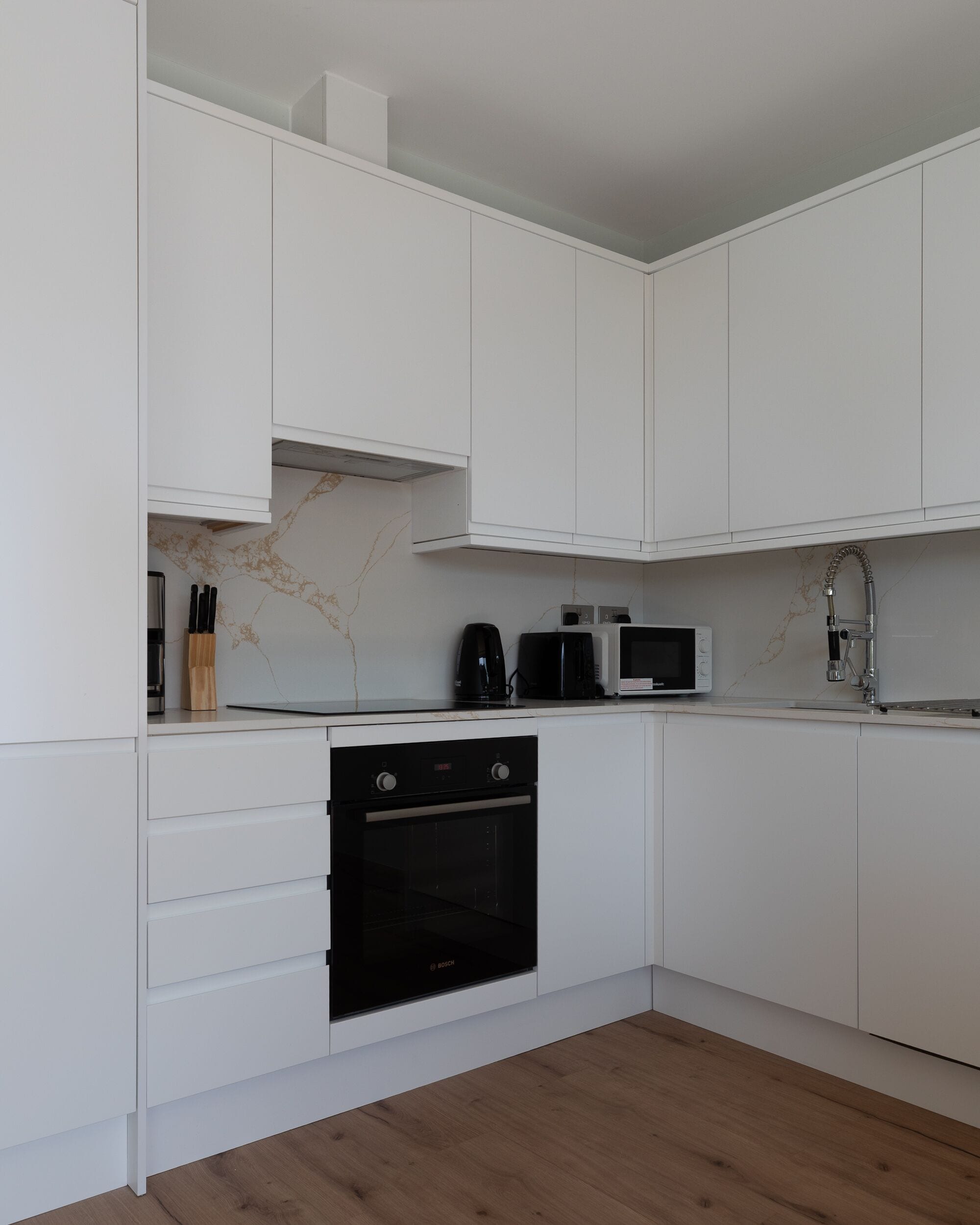 Eine moderne Küche mit weißen Schränken, einem Bosch-Ofen, einer Mikrowelle und einer Kaffeemaschine.