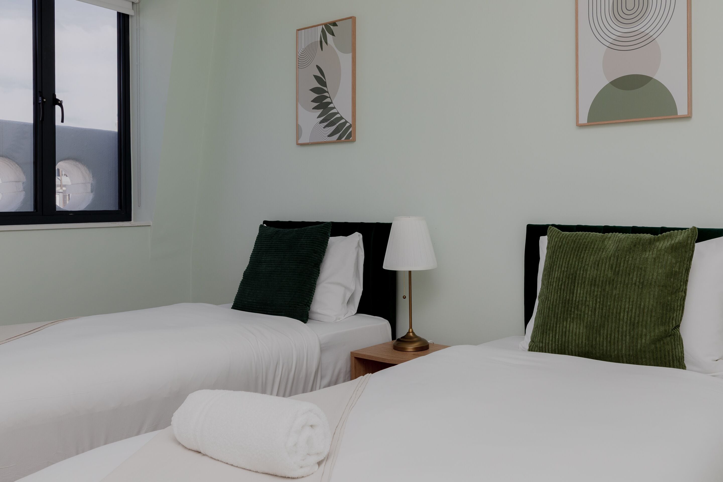A hotel room with two beds, a window, and artwork on the wall.