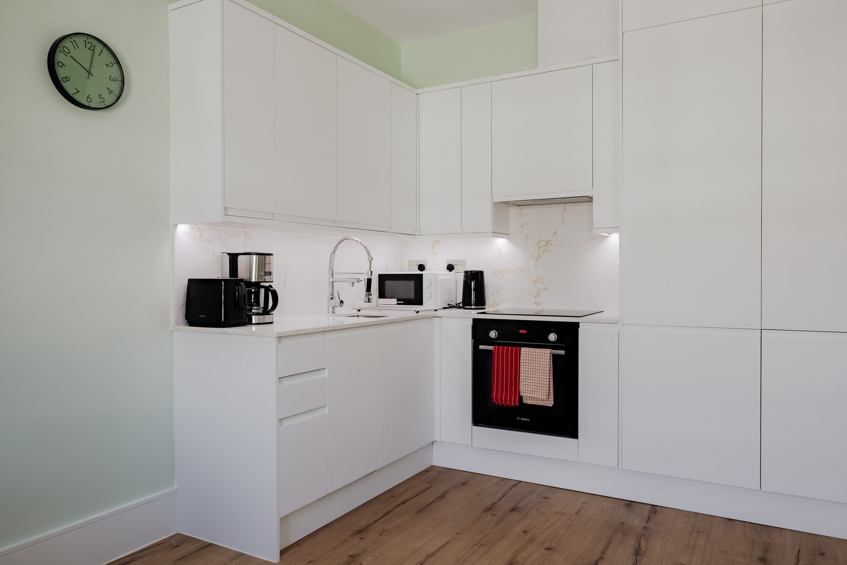 Eine moderne Küche mit weißen Schränken, einer Kaffeemaschine, einer Mikrowelle und einem Backofen.