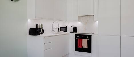 Eine moderne Küche mit weißen Schränken, einer Kaffeemaschine, einer Mikrowelle und einem Backofen.