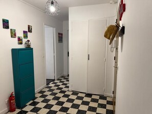 A hallway with a teal cabinet, a fire extinguisher, a checkered floor, and a door with a basket on the wall.