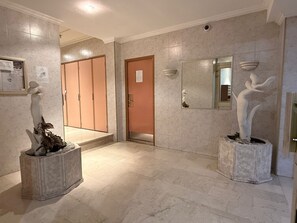 Un couloir doté d’un sol en marbre, d’une porte en bois et de deux sculptures posées sur des piédestaux.