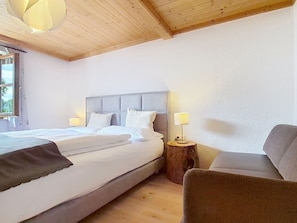 Ein Schlafzimmer mit einem Bett, Nachttischlampen, einem Sessel und einer Holzbalkendecke.