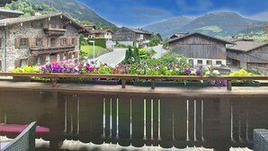 Un pueblo de montaña con casas de madera tradicionales, un camino sinuoso y un balcón con flores.