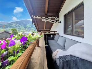 Ein Balkon mit Holzgeländer, einem grauen Sofa und einem Korbstuhl.