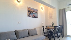 Un salon moderne avec un canapé gris, une table ronde en bois et un coin repas avec des chaises noires.