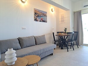 Ein modernes Wohnzimmer mit einem grauen Sofa, einem runden Holztisch und einem Essbereich mit schwarzen Stühlen.