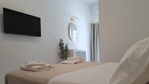 Une chambre à coucher avec un lit, un téléviseur à écran plat fixé au mur, un miroir et une plante en pot.