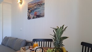 Une table à manger avec un panier de fruits, un plateau en osier contenant des condiments et un tableau accroché au mur.