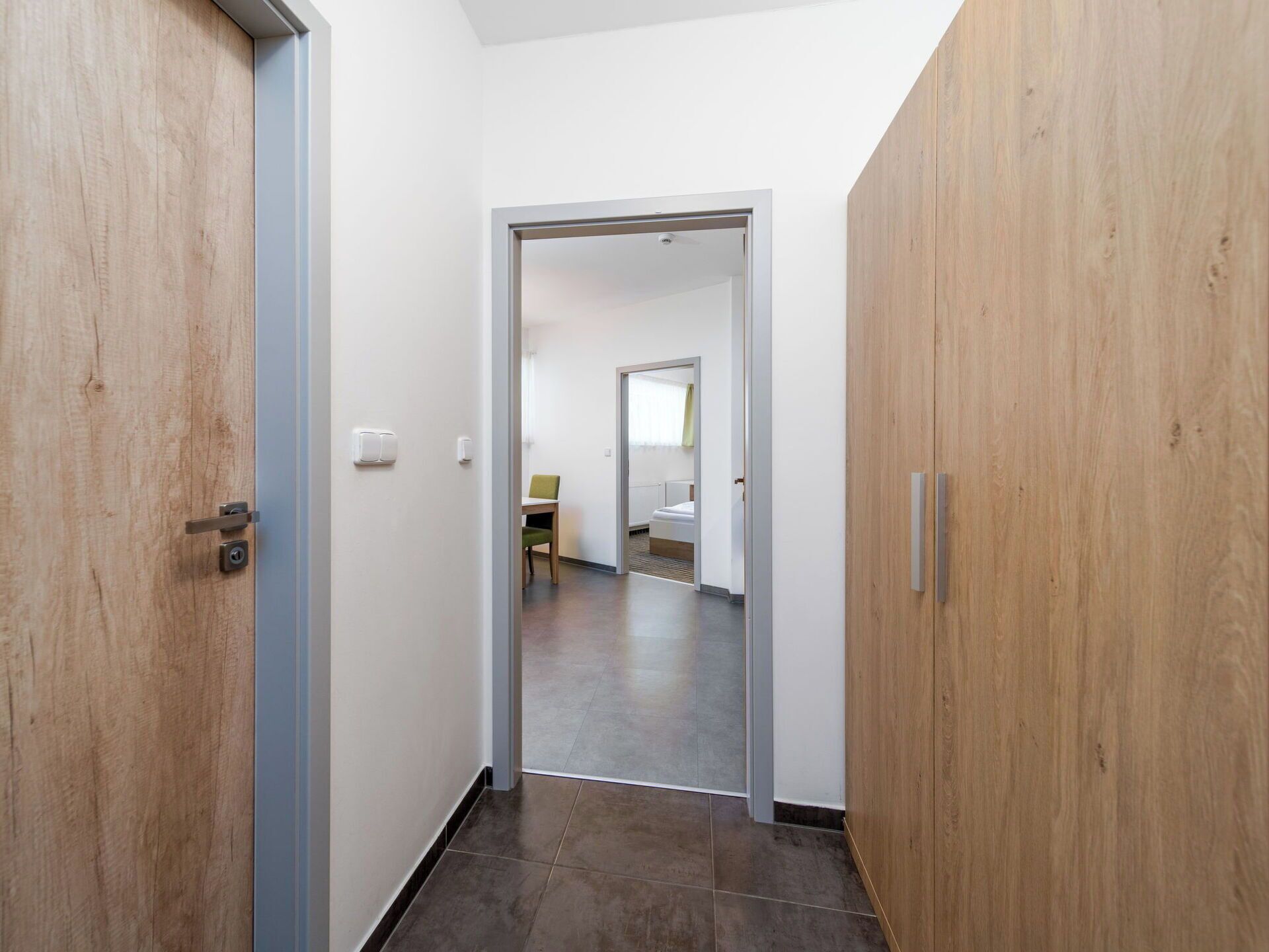 Un corridoio con porte in legno, un letto in vista e una sedia nella stanza adiacente.
