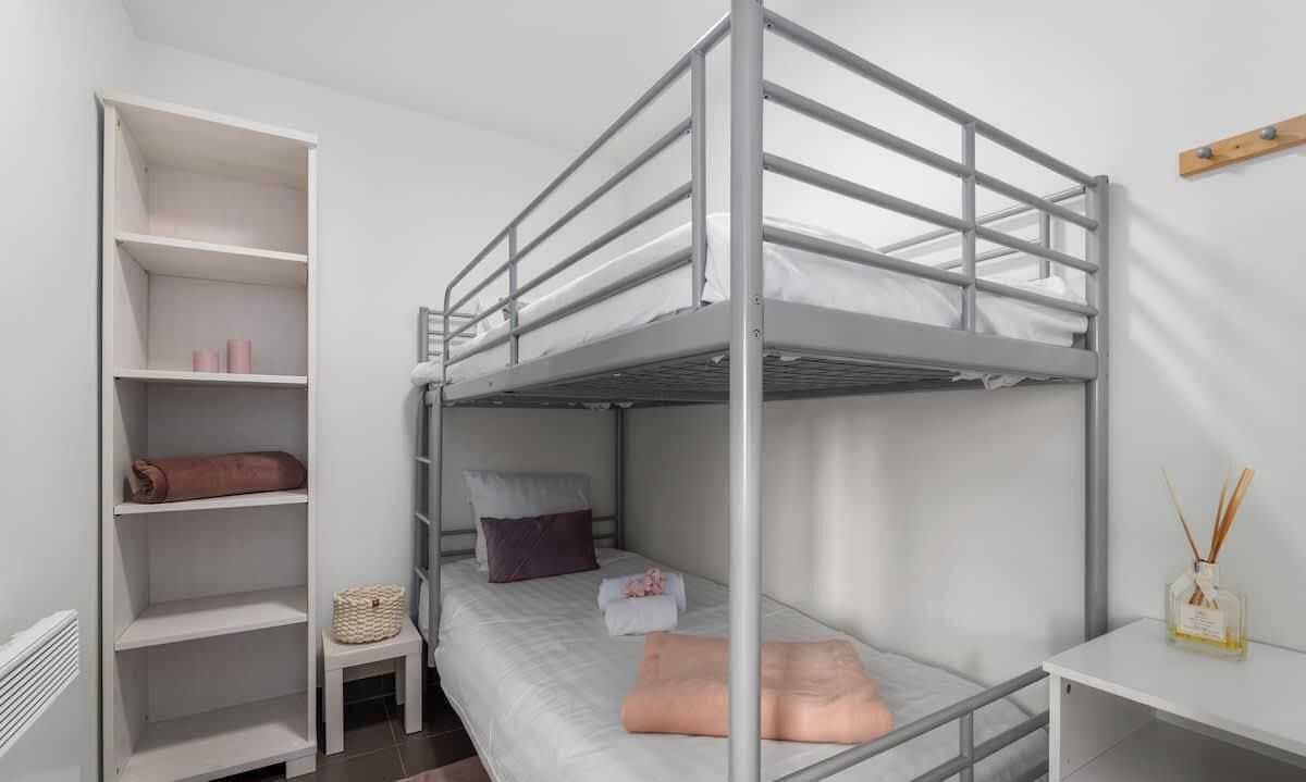 Ein Schlafzimmer mit Etagenbetten, einem weißen Kleiderschrank, einem kleinen Tisch und einem an der Wand befestigten Regal.