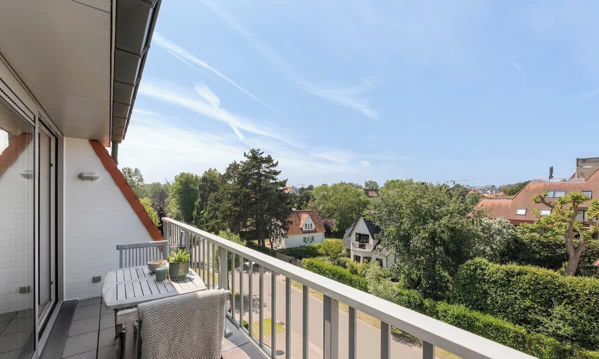 En balkon med et bord og stole, der ud til et boligområde med huse og træer.