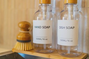 Zwei Glasflaschen mit dem Aufdruck 'HAND SEIFE' und 'SPÜLMITTEL', daneben eine Holzbürste.