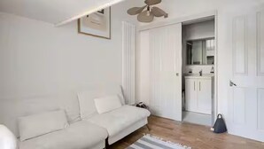 Ein modernes Wohnzimmer mit einer Couch, einem Deckenventilator und Blick ins Badezimmer.