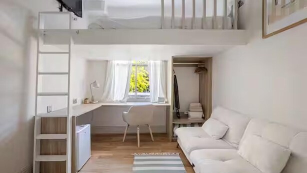 Ein kleines Zimmer mit einem Etagenbett, einem Schreibtisch, einem Stuhl und einem weißen Sofa.