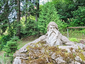 Eine steinerne Statue eines bärtigen Mannes auf einem moosbewachsenen Felsen in bewaldeter Landschaft.