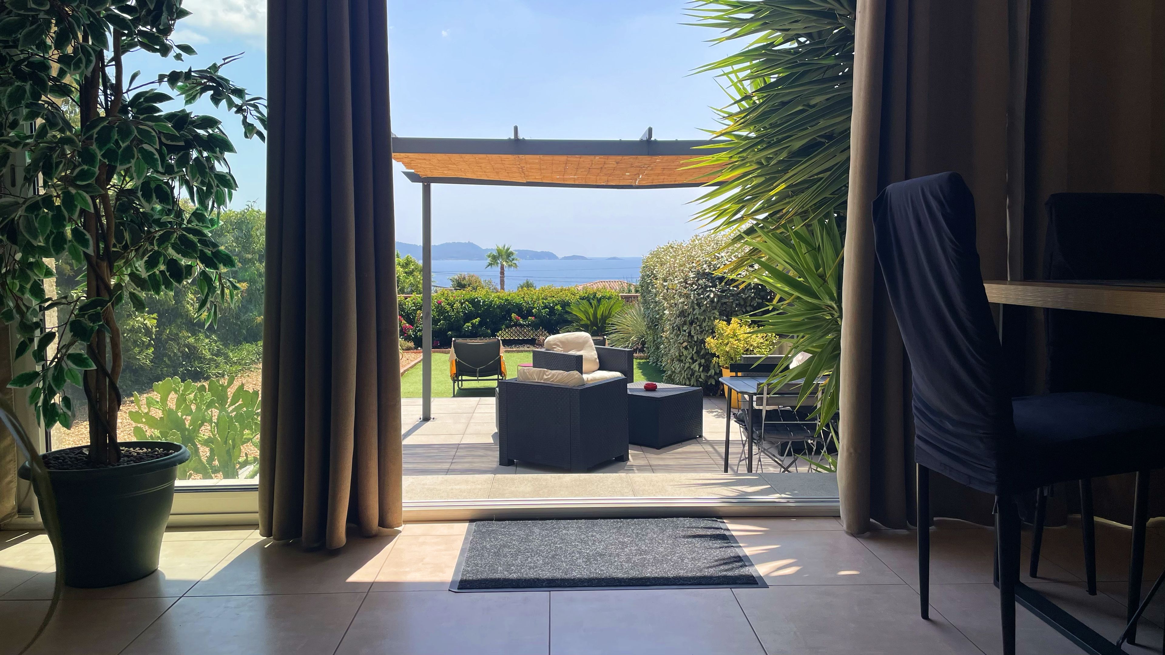 Une chambre avec vue sur la mer, une terrasse avec des meubles d’extérieur et une grande fenêtre avec des rideaux.
