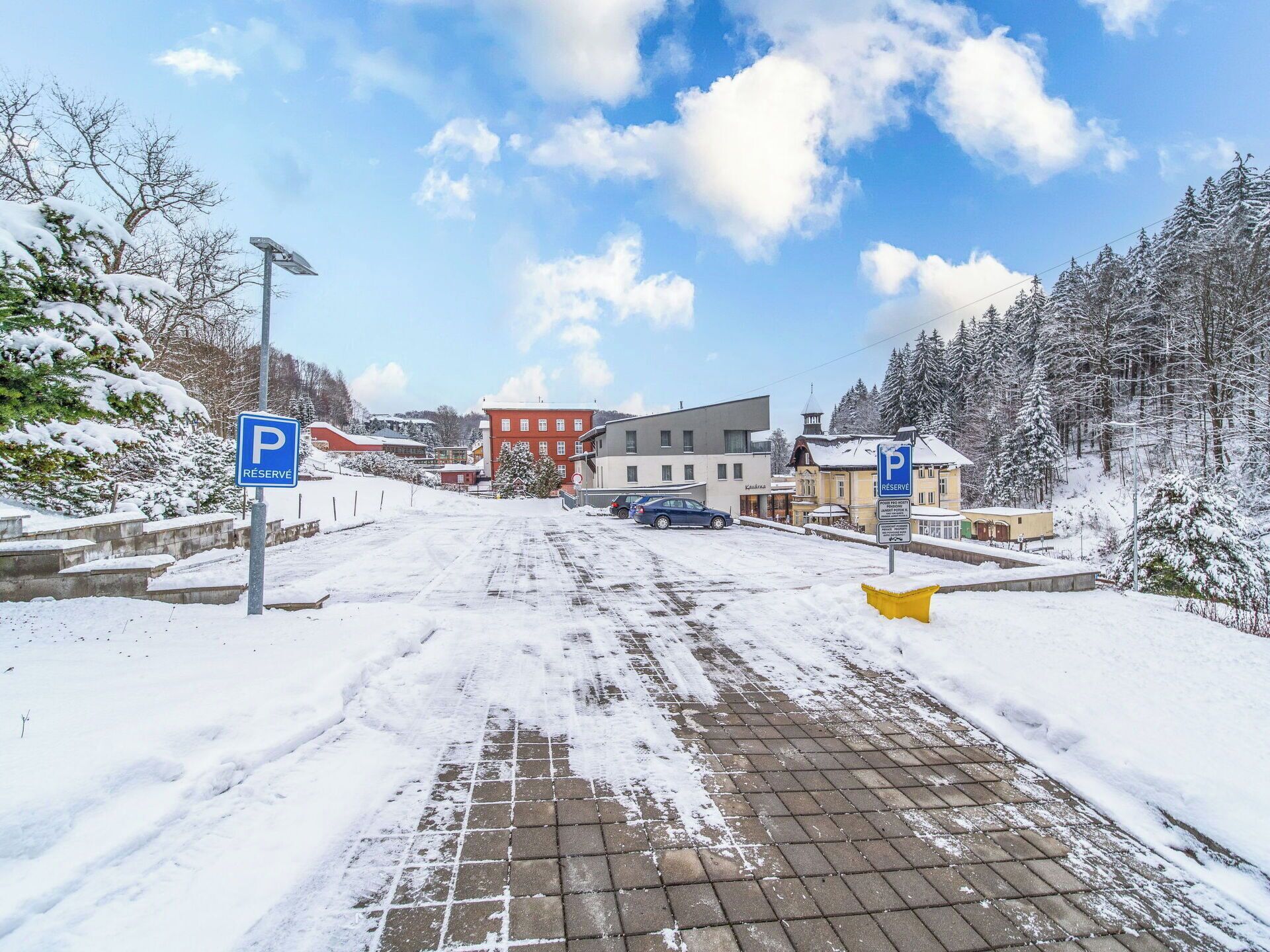 A snowy parking area with a paved walkway leading to buildings.