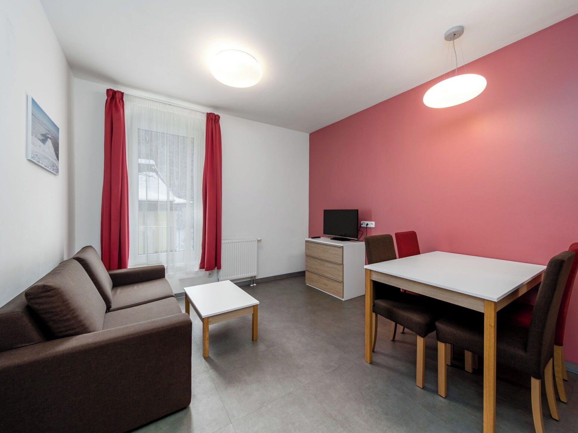 Een moderne kamer met een bank, een eettafel met stoelen, een tv op een dressoir en een raam met gordijnen.