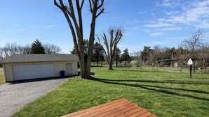 Un jardin avec une terrasse en bois, un garage et un arbre.