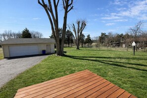 A backyard with a wooden deck, a garage, and a tree. - Cozy home with fenced yard (Bowling Green)