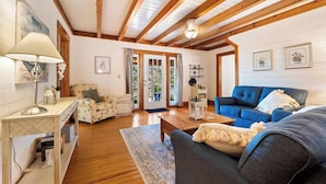 Ein gemütliches Wohnzimmer mit Holzbalken, einem blauen Sofa, einem weißen Sessel, einem Holztisch und einer Lampe.