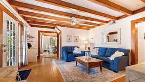 Amplia sala de estar con vigas de madera, un sofá azul, una mesa de centro y un comedor al fondo.