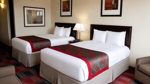 A hotel room with two beds, a nightstand, a lamp, and a chair.
