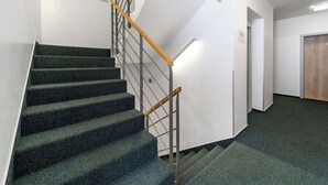 Eine Treppe mit hölzernem Geländer, Teppichstufen und einer weißen Wand mit einer Tür und einem Schild.