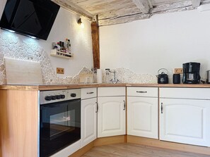 A kitchen with a built-in oven, white cabinets, a wooden countertop, a black stove, and a wall-mounted TV.