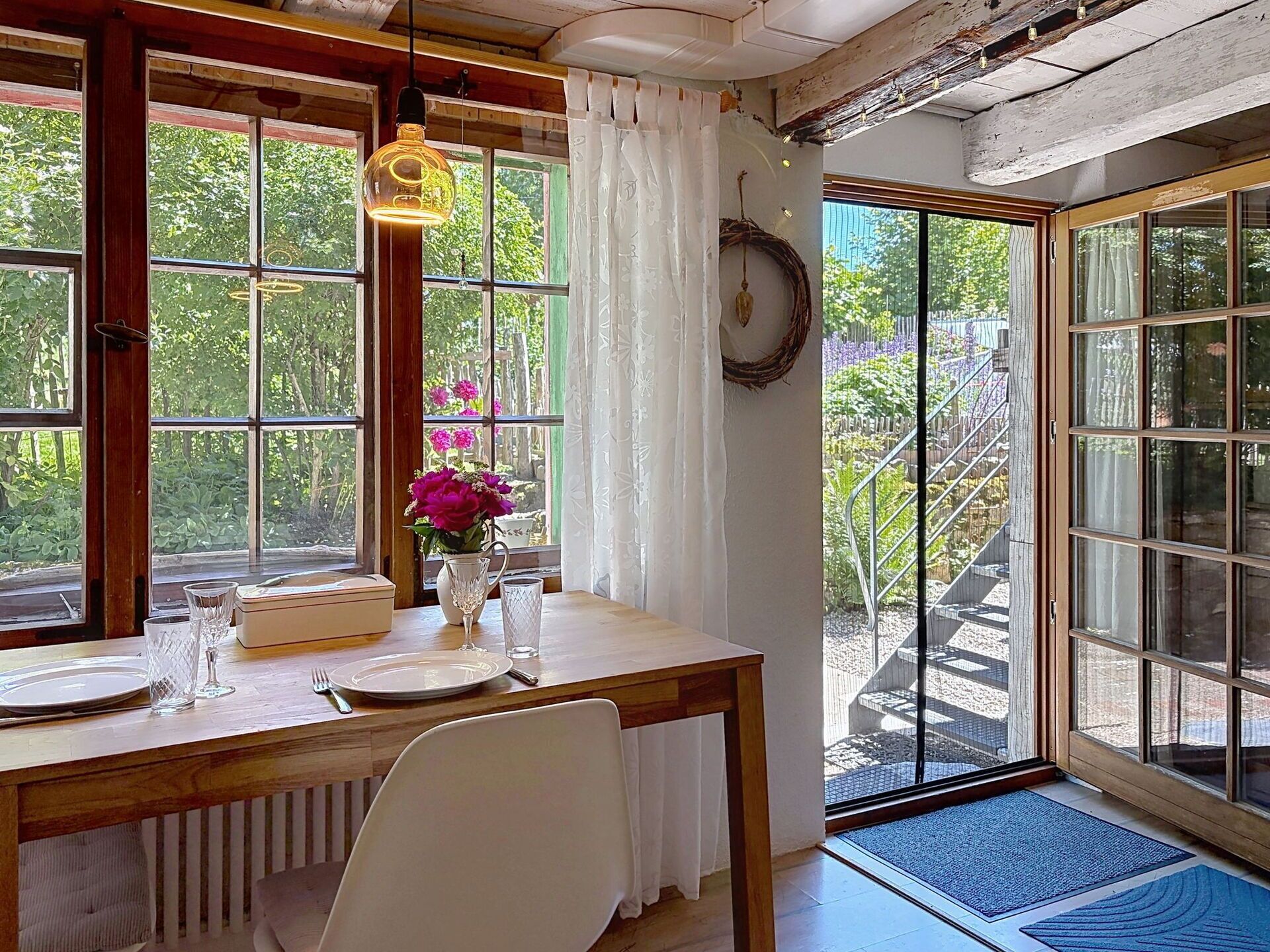 Ein Essbereich mit Tisch für zwei Personen, einer Blumenvase und Blick ins Freie durch große Fenster.