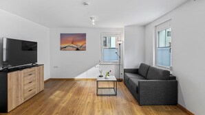 Ein modernes Wohnzimmer mit Flachbildfernseher, Holzschränken, einem grauen Sofa, einem Couchtisch und einem Sonnenuntergangsbild.