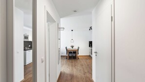 Ein schmaler Korridor mit Holzboden, weißen Wänden und einem Essbereich mit Tisch und Stühlen.