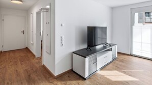 Eine moderne Wohnung mit Flachbildfernseher auf einem Schrank, Holzboden, weißen Wänden und einer Tür zu einem weiteren Raum.