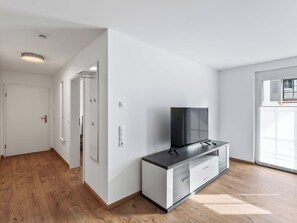 A modern apartment with a flat-screen TV on a cabinet, wooden flooring, white walls, and a door leading to another room. - Nice apartment for 3 guests with WIFI and TV (Endingen)