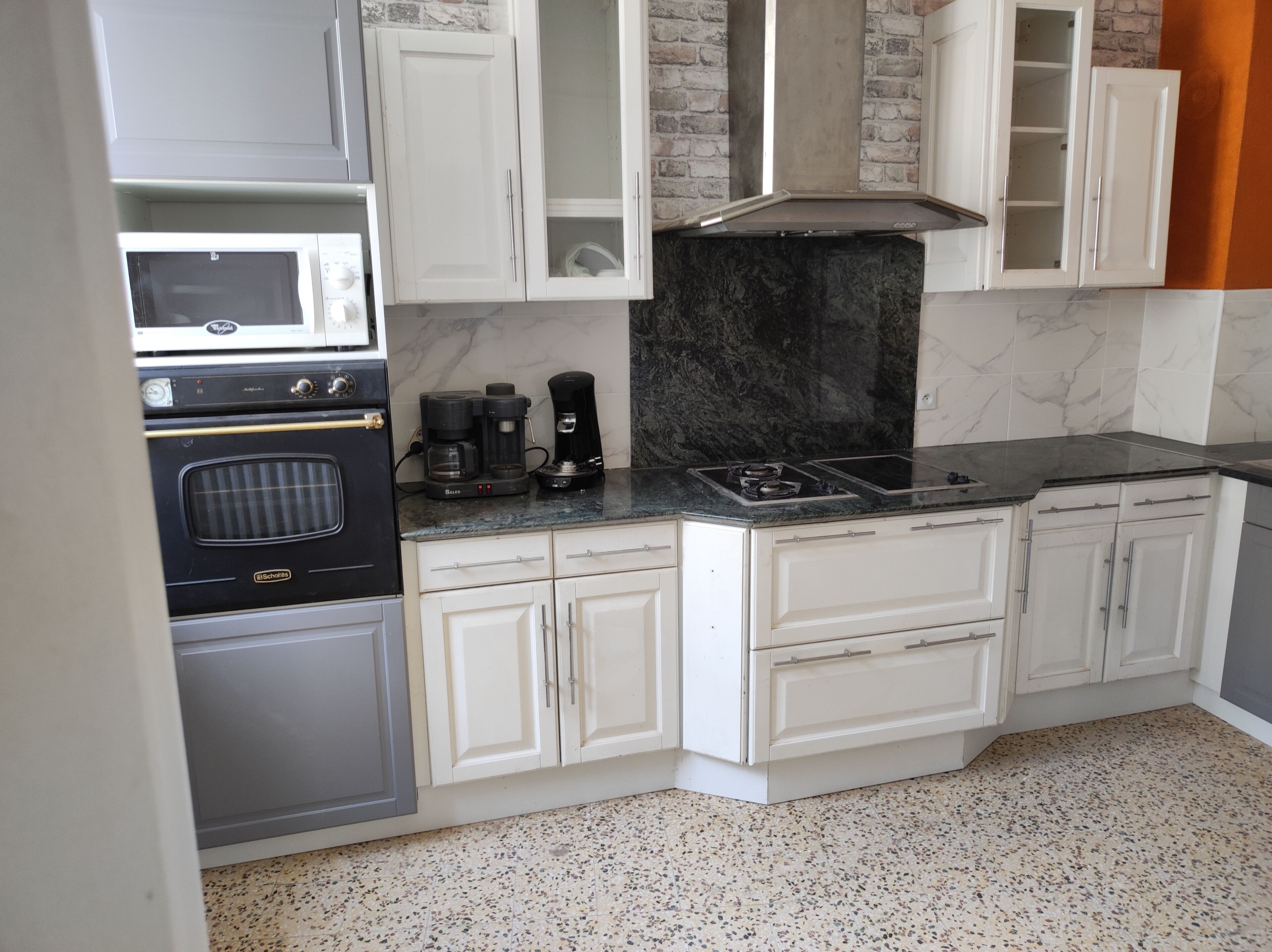 Una cocina con gabinetes blancos, una estufa negra, una cafetera y un microondas.