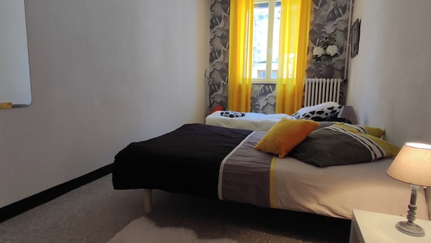 Ein Schlafzimmer mit zwei Betten, einem Heizkörper, einer Lampe und einem Fenster mit Vorhängen.