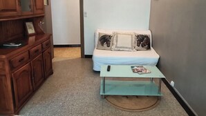 Ein kleines Zimmer mit einer Couch, einem Holzschrank, einem kleinen Tisch und einer Wandleuchte.