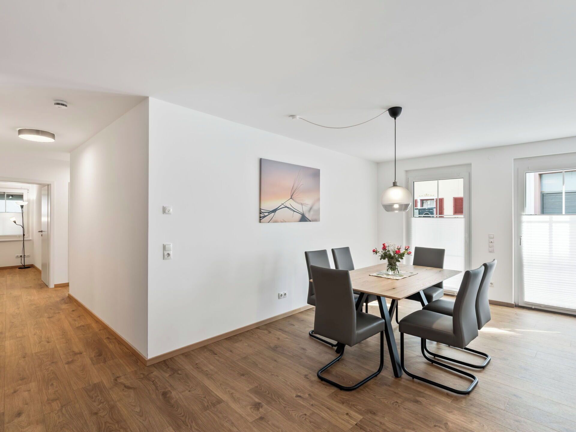 Een moderne eetruimte met een houten tafel, zes stoelen, een hanglamp en een wanddecoratie.