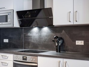 Eine moderne Küche mit Edelstahlgeräten, darunter eine Mikrowelle, ein Backofen und ein Herd, mit Spritzschutz und Schränken.