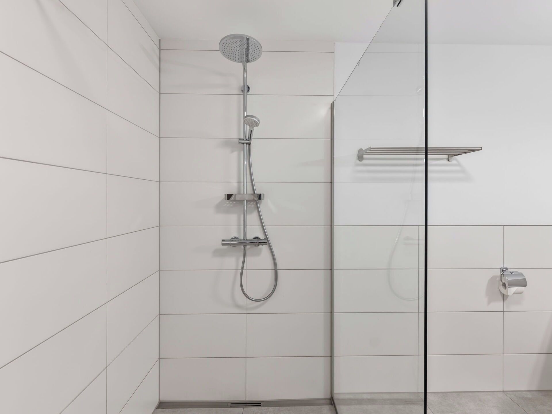 Une douche moderne dotée d’un pommeau de douche à main, d’un robinet mural et d’un espace de douche délimité par des parois en verre.
