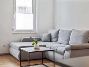 A modern living room with a grey sofa, a small black metal table, and a white vase with flowers. - Cosy apartment for 5 people with WIFI, TV, terrace and pets allowed (Endingen)