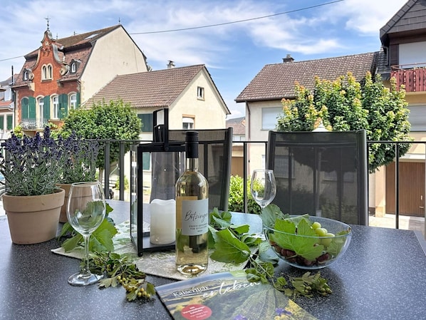 Une table dressée à l’extérieur, avec une bouteille de vin, des verres et un saladier de raisins.